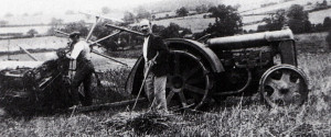 This is the second tractor on the farm with the wide, flowing mudguards. The exhaust want under the rear axle as on the later green model. Kenneth Orchard's father is working on the string box of the Massey Harris binder.