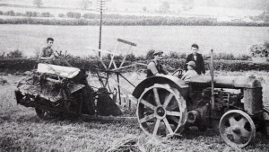 Kenneth Orchard wonders what the health and safety would make of this picture. His father is driving, Kenneth is sitting on the mudguard, his brother is sitting on the pile of sacks, and on the McCormick binder (which the string box fell off) is his cousin. This was the orange tractor, and the cleats look almost worn out, but spade lugs were fitted later.