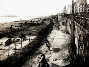 A fortified Brighton sea front during the Second World War, with barbed wire on both upper and lower esplanades, rows of beach defences and a pier deliberately cut in half.