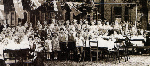 Partying on VE Day 1945, showing the horse chestnut trees and grassed area, with the author in a jester’s suit at the extreme right end of the table.